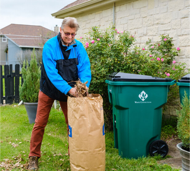 Waste service representative with tablet standing by a commercial trash dumpster.