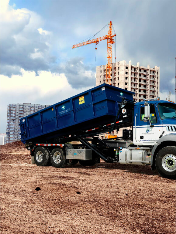 A man rolls two residential trash carts to the curb as a Waste Connections garbage truck approaches for pickup